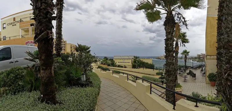 Kerti sétány a Corinthia St George's Bay területén, balra a szállodaépület, a háttérben a tenger
