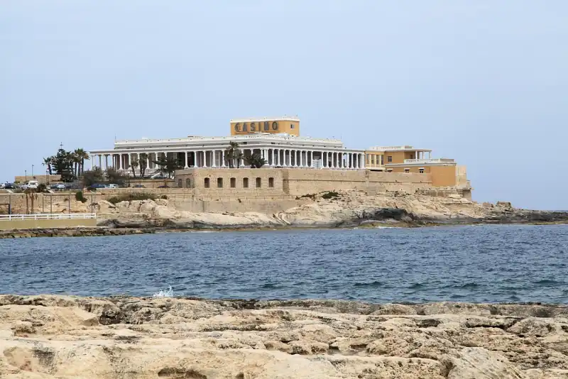 Az oszlopsoros Dragonara-palota CASINO felirattal, a vízen át nézve a Dragonara-félszigeten